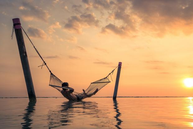 Greenock Telegraph: A man relaxing over the water in a hammock. Credit: Canva